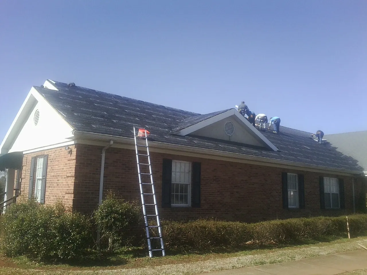 Crew tearing shingles off a brick ranch roof with a ladder set — Emergency Roof Repair work by our crew in Kingwood