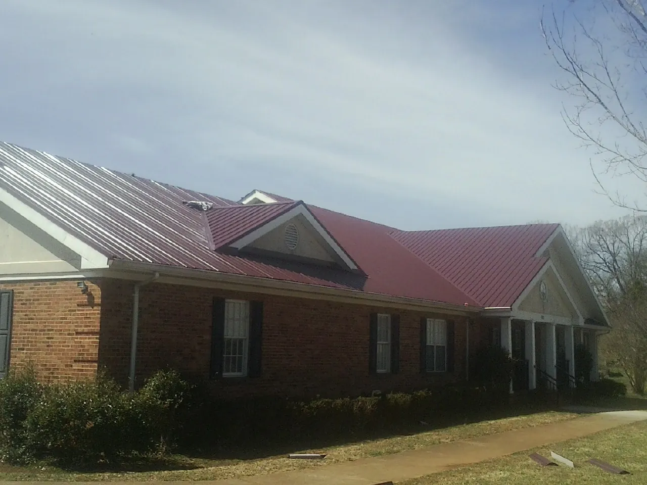 Red metal roof with gabled entries on a long brick building, from a Hail Damage Roof Repair job in Kingwood