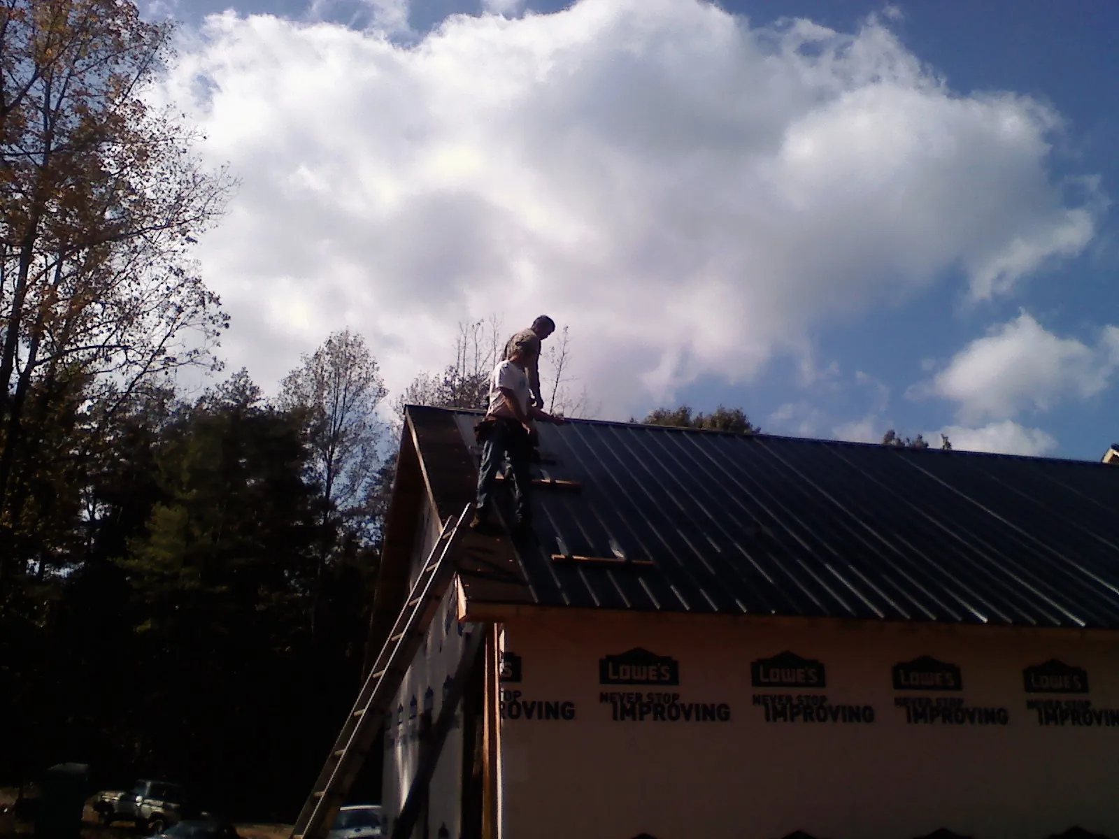 Roofer fastening dark metal panels high against a cloudy sky in Kingwood