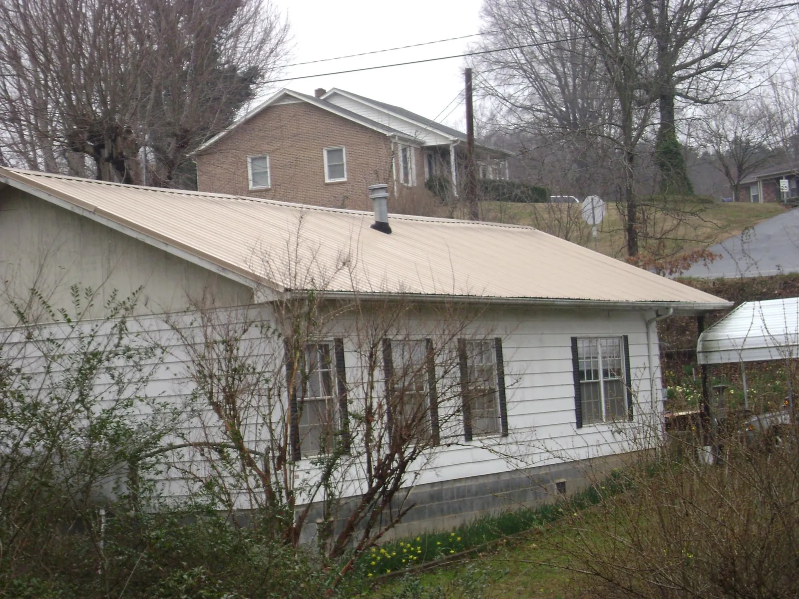 Tan metal roof on a white sided house set into a hillside — Commercial Roofing by Roofing Brothers in Kingwood